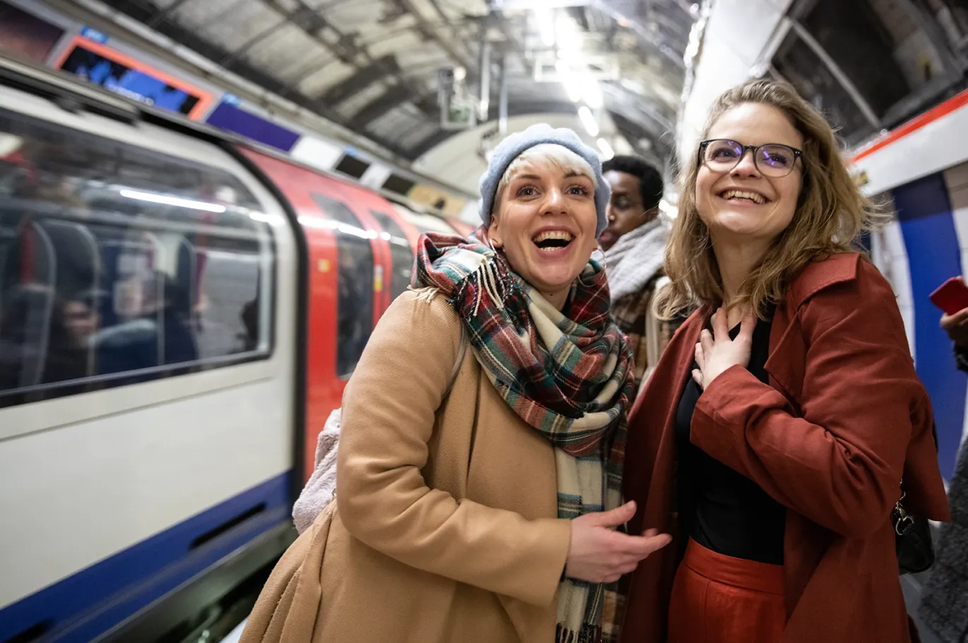 Two women smiling together while traveling on a metro train.