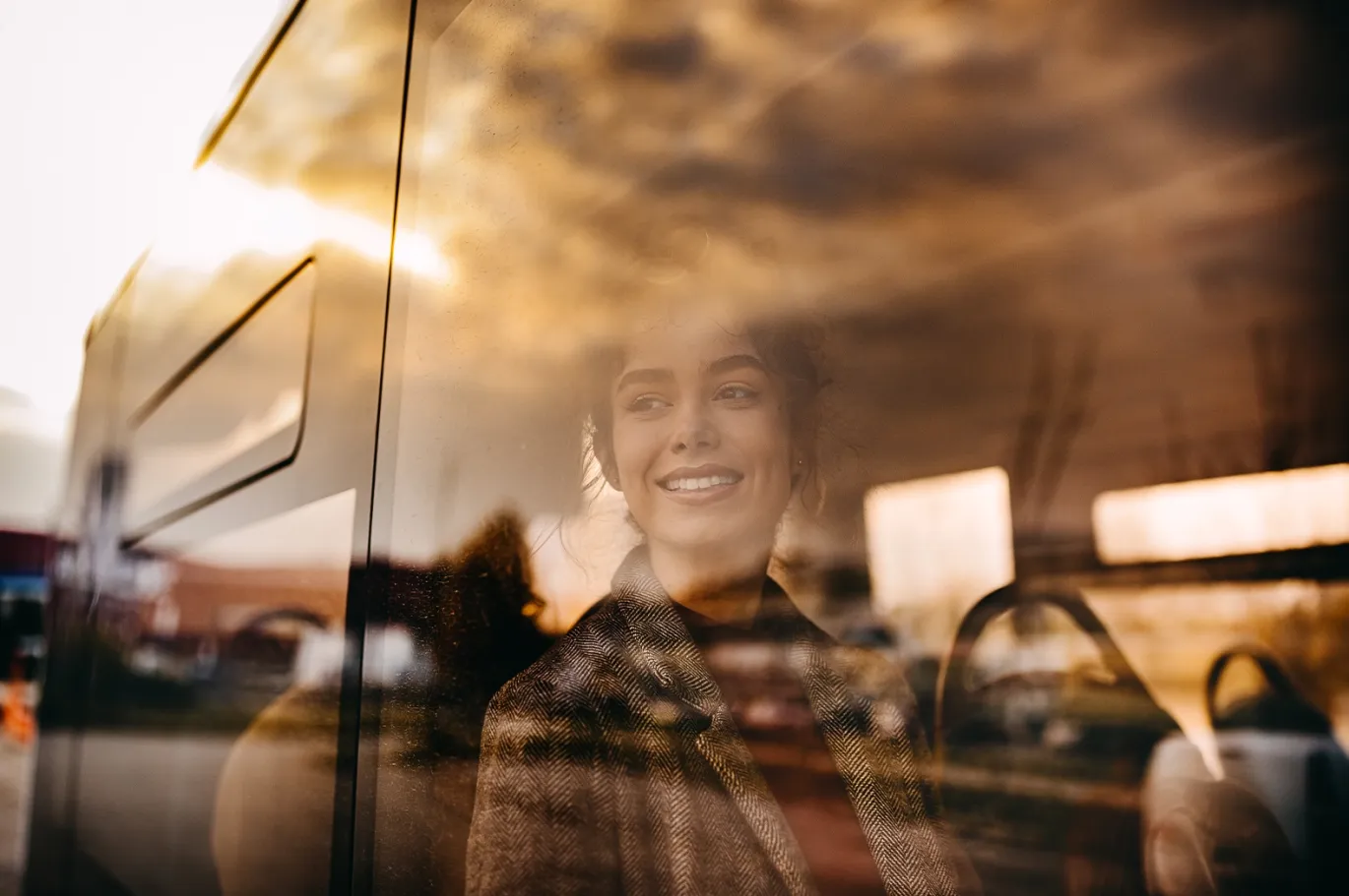 Young woman smiling while traveling on a bus during sunset.