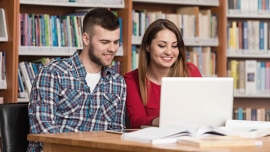 A man and a woman study using a laptop in  the library
