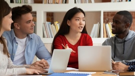 Four students sitting at the table with computers 