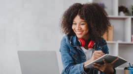 young woman writing on a pad and looking at laptop