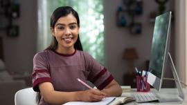 Lady at desk with computer and notebook smiling at camera