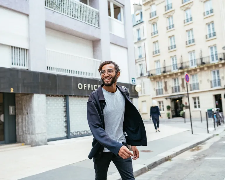 A man in a black jacket smiling and walking in the European streets