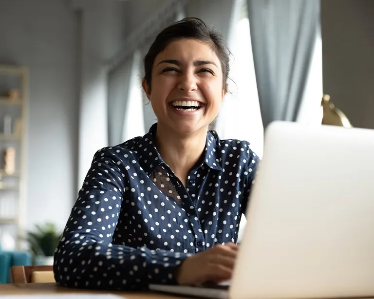 Woman smiling while attending an online IELTS study session on her laptop