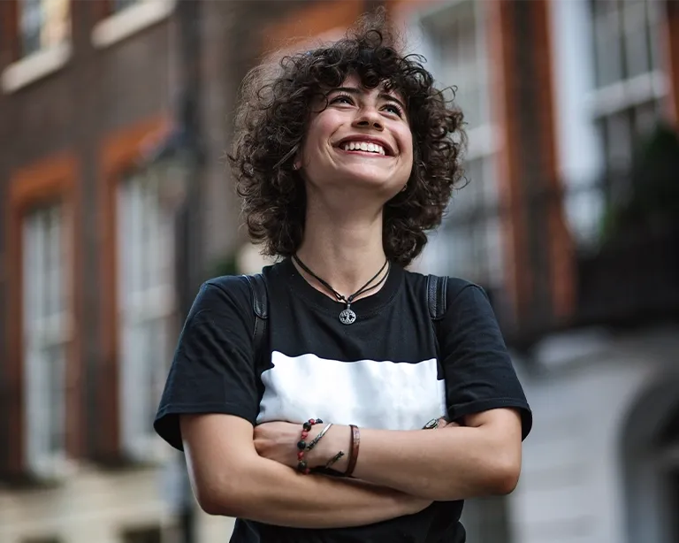 Young person with curly hair smiling outdoors