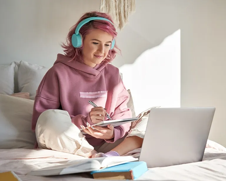 A girl taking notes while studying for IELTS exam online