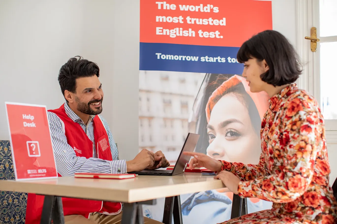 IELTS test taker speaking with an IELTS examiner at an IELTS test center reception desk