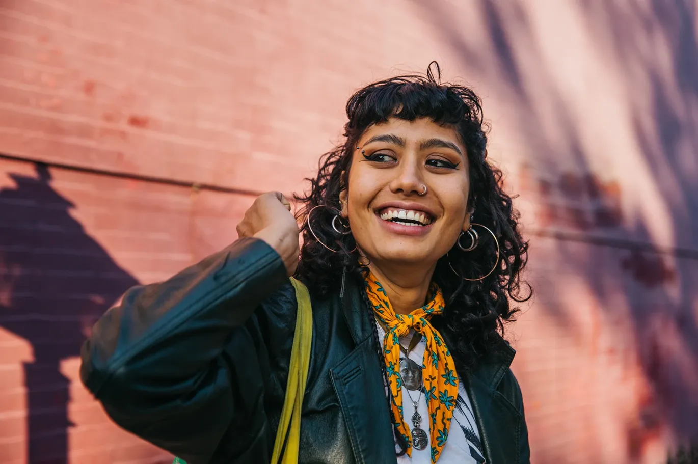 Smiling young woman with curly hair standing at IELTS test center with a shoulder bag