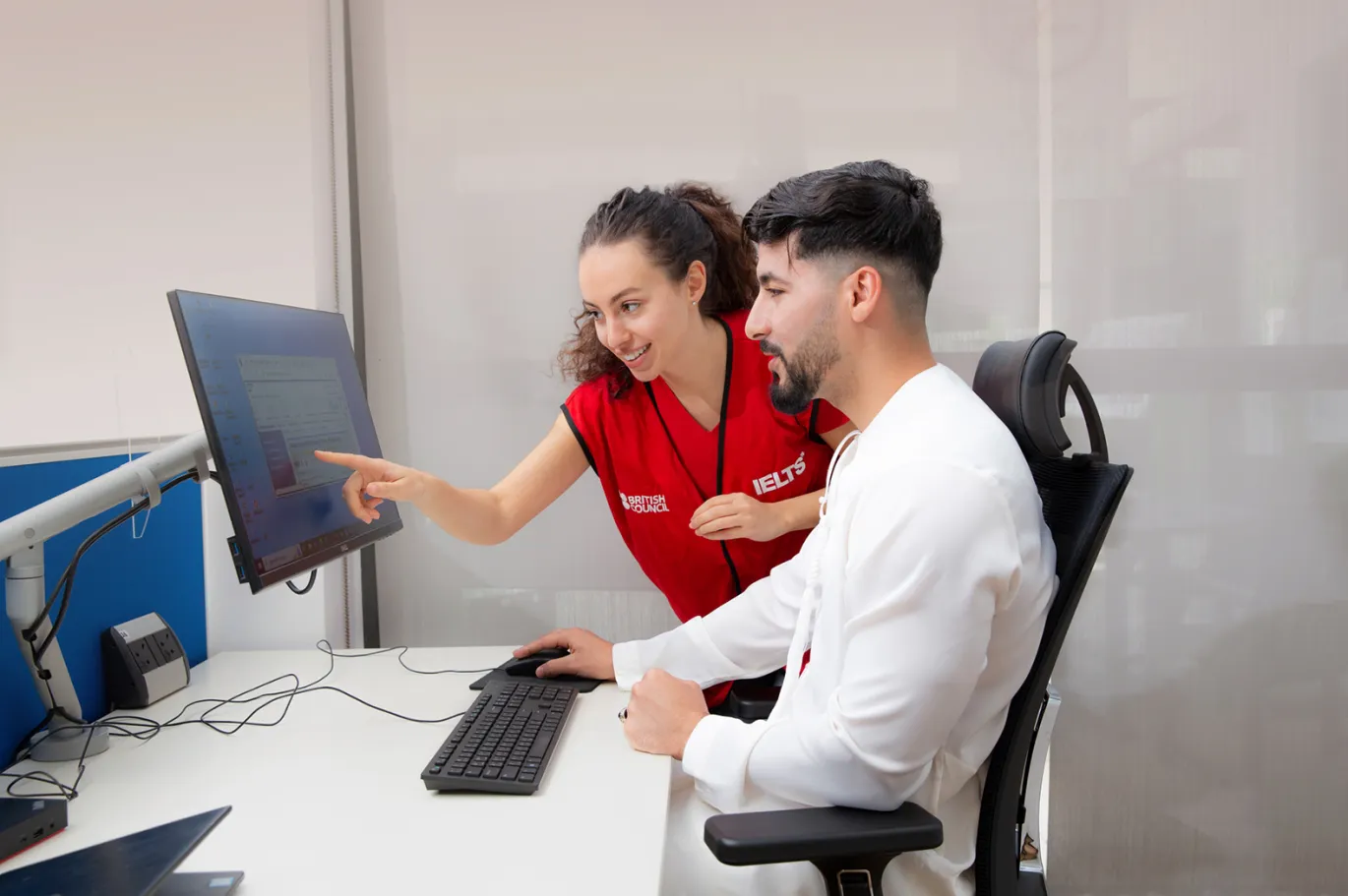 Two students reviewing IELTS exam preparation materials together on a computer in a study center