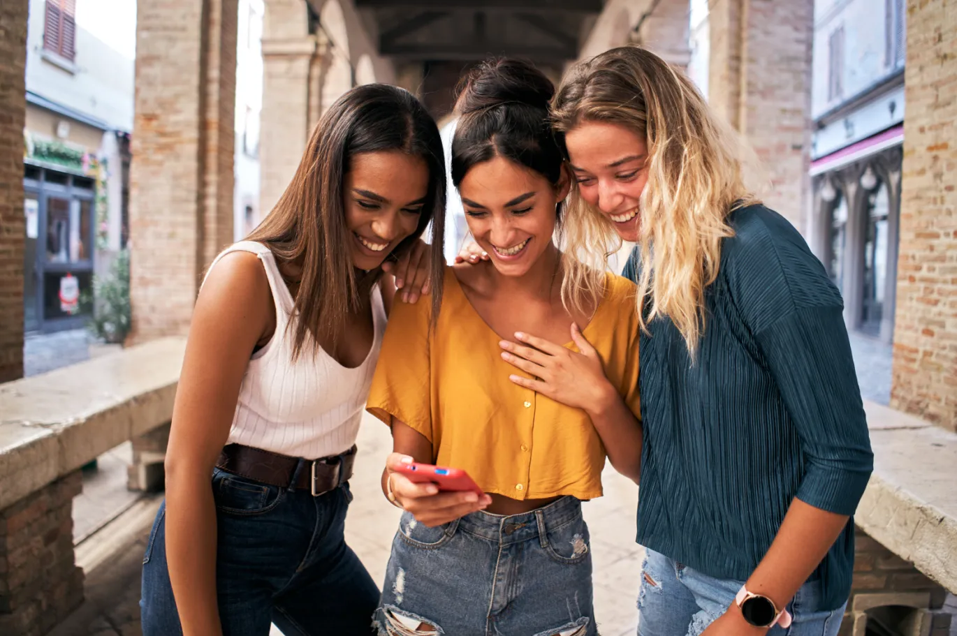 Three friends smiling while looking at a mobile phone together.