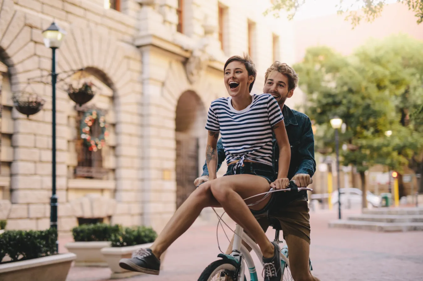 Two friends riding a bicycle together through a European city street.