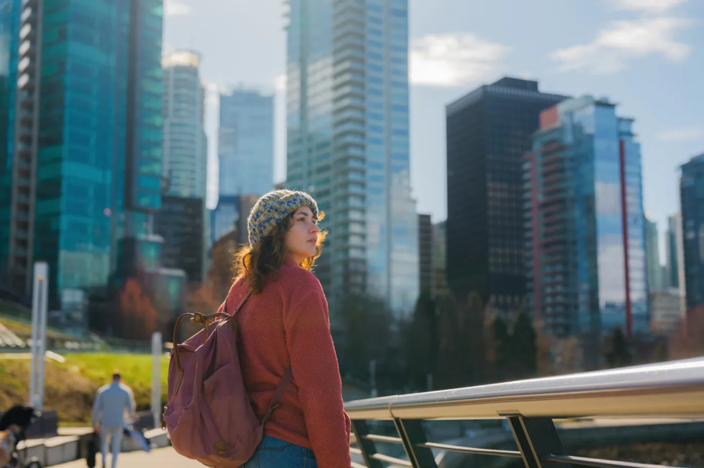 Young woman with a backpack standing in a modern city with high-rise buildings