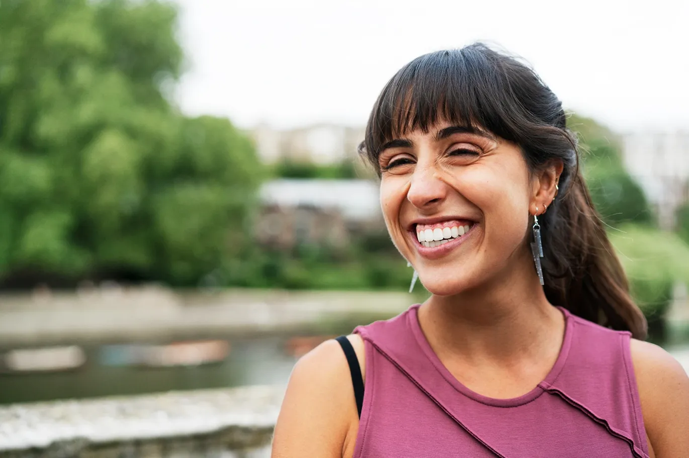 Young woman with a backpack smiling outdoors near a waterfront
