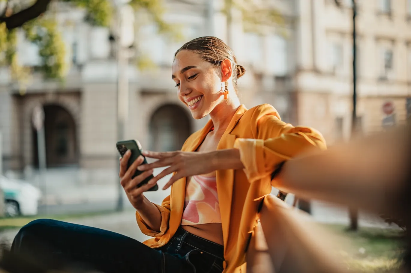 Young woman smiling while checking her phone outdoors on a sunny day