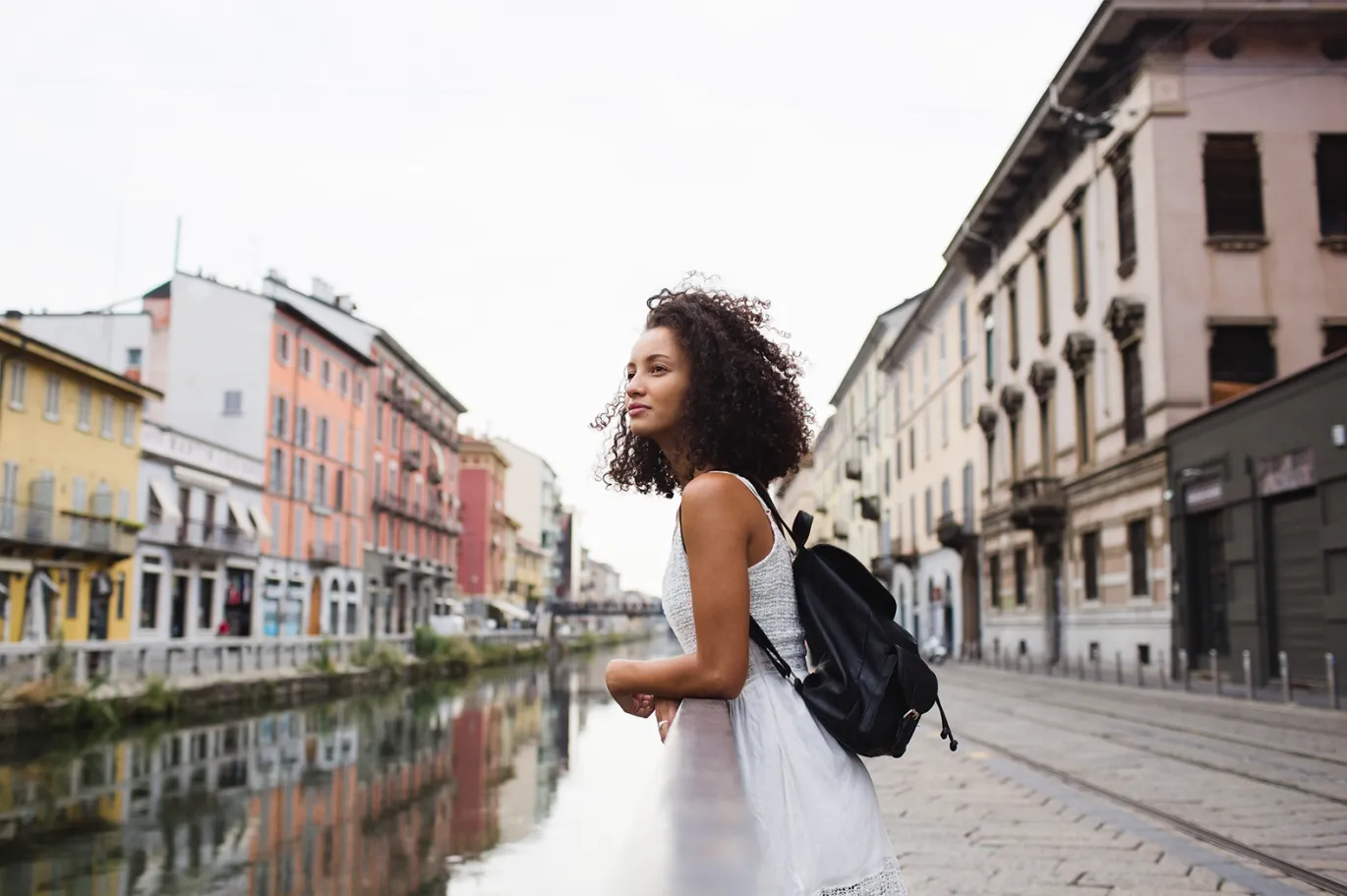 Young woman with curly hair and a backpack walking beside a canal in a European city