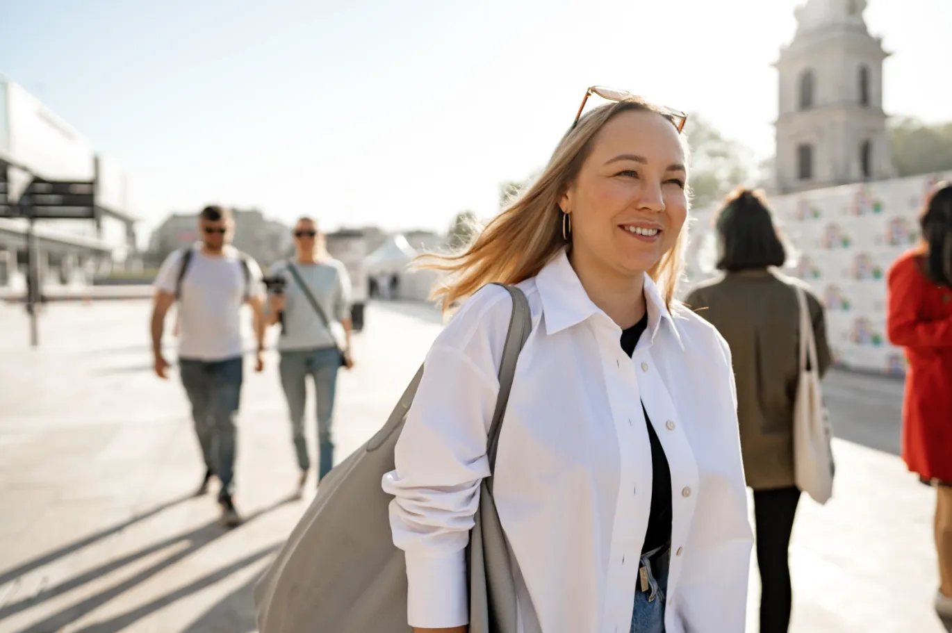 Young woman walking through a city street with a shoulder bag on a sunny day