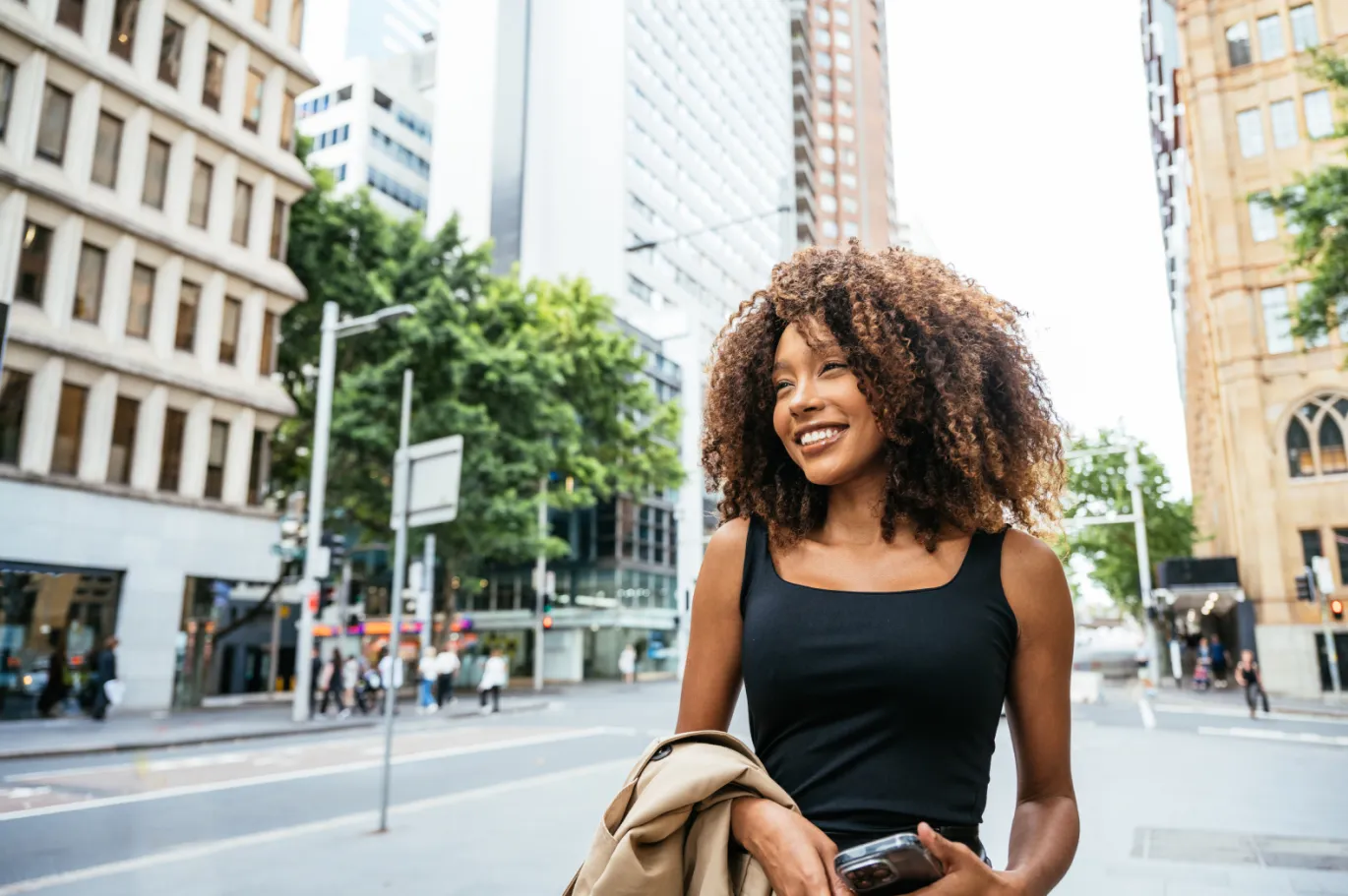 Curly hair girl walking throught the street with a coat in her hand.