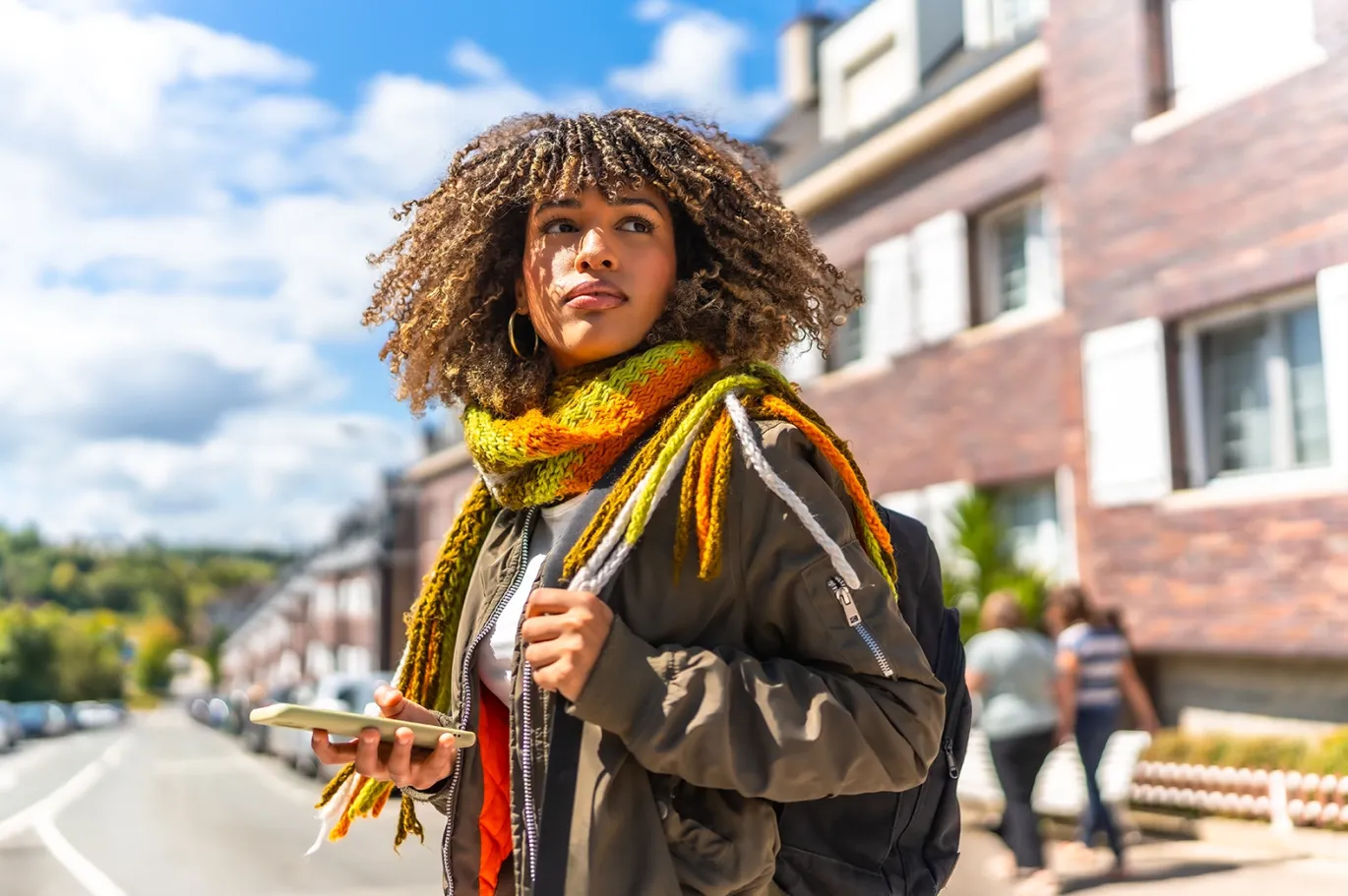 Curly-haired young woman with a backpack walking outdoors on a sunny day.