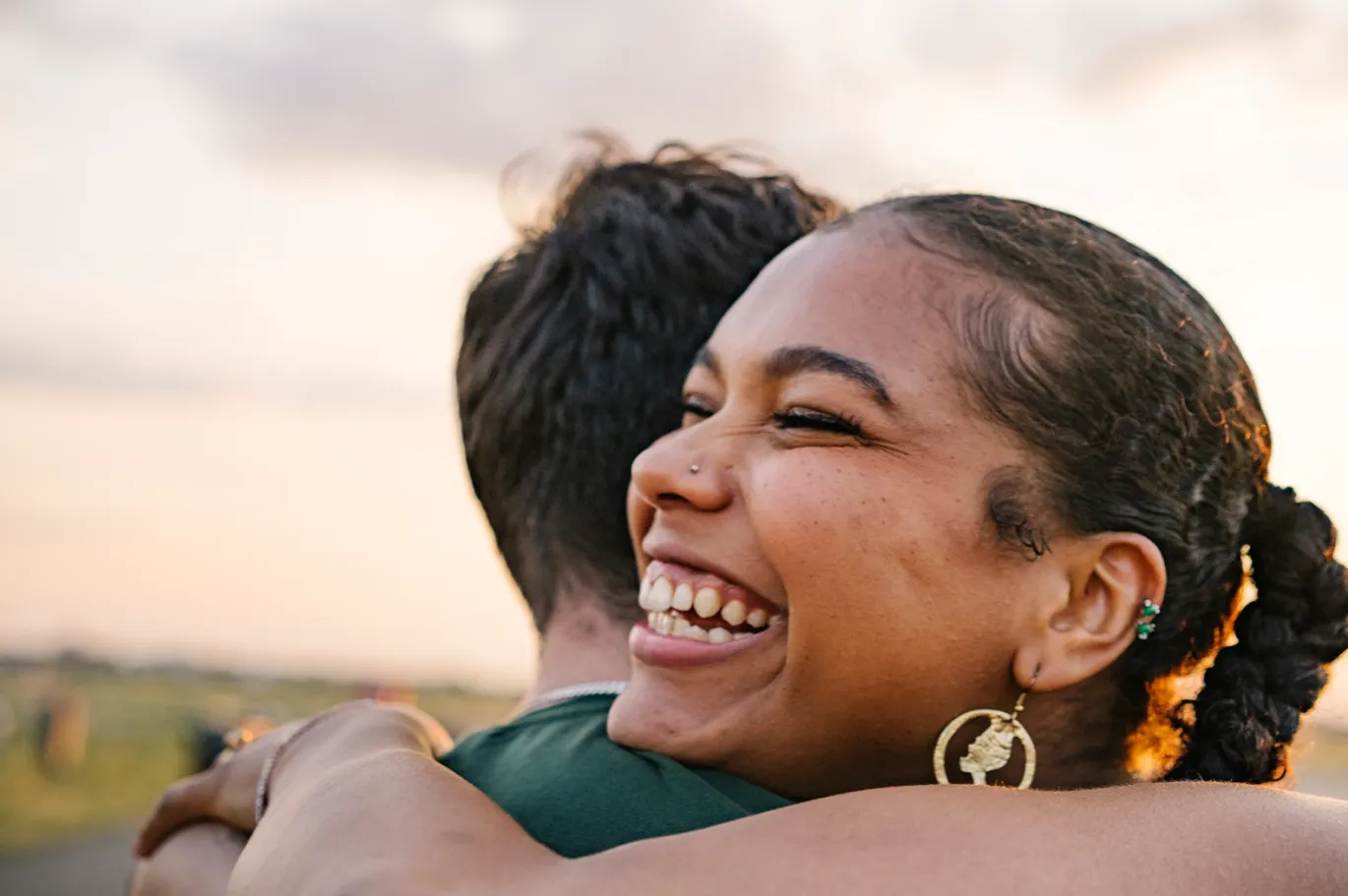 Two friends sharing a joyful hug outdoors during sunset.