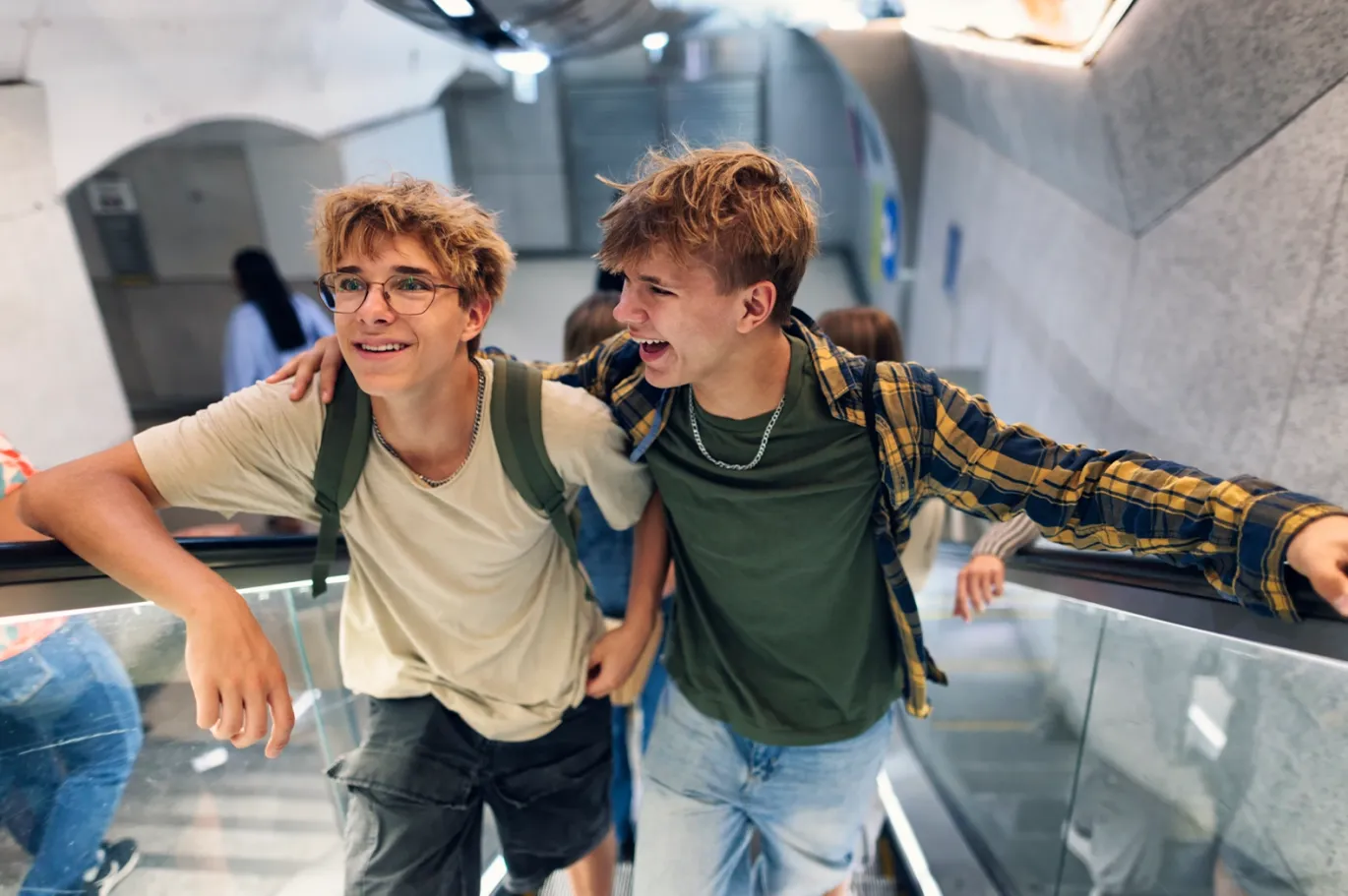 Two friends smiling together while riding an escalator indoors.