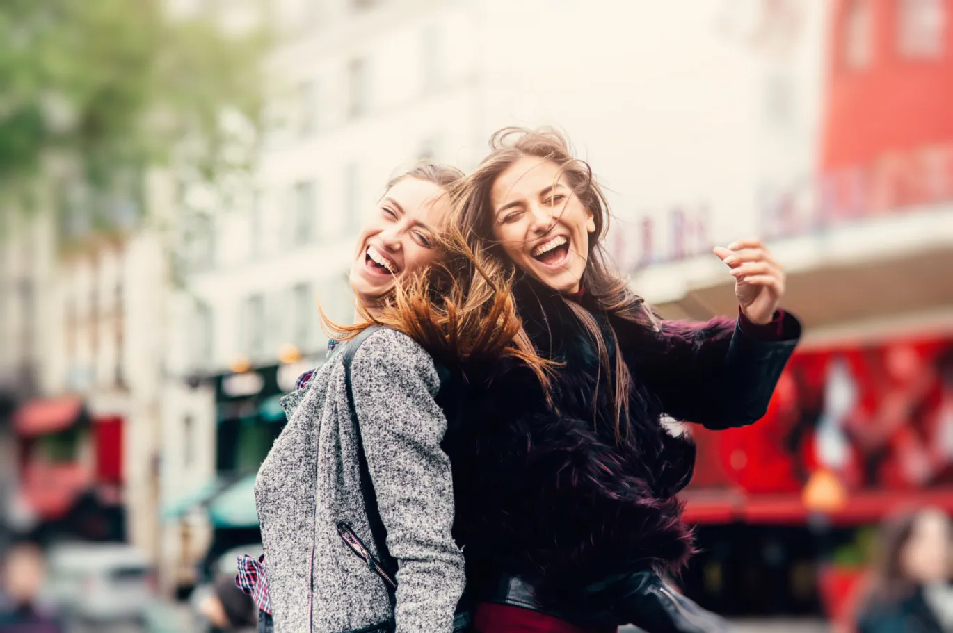 Two friends smiling and posing together on a city street.