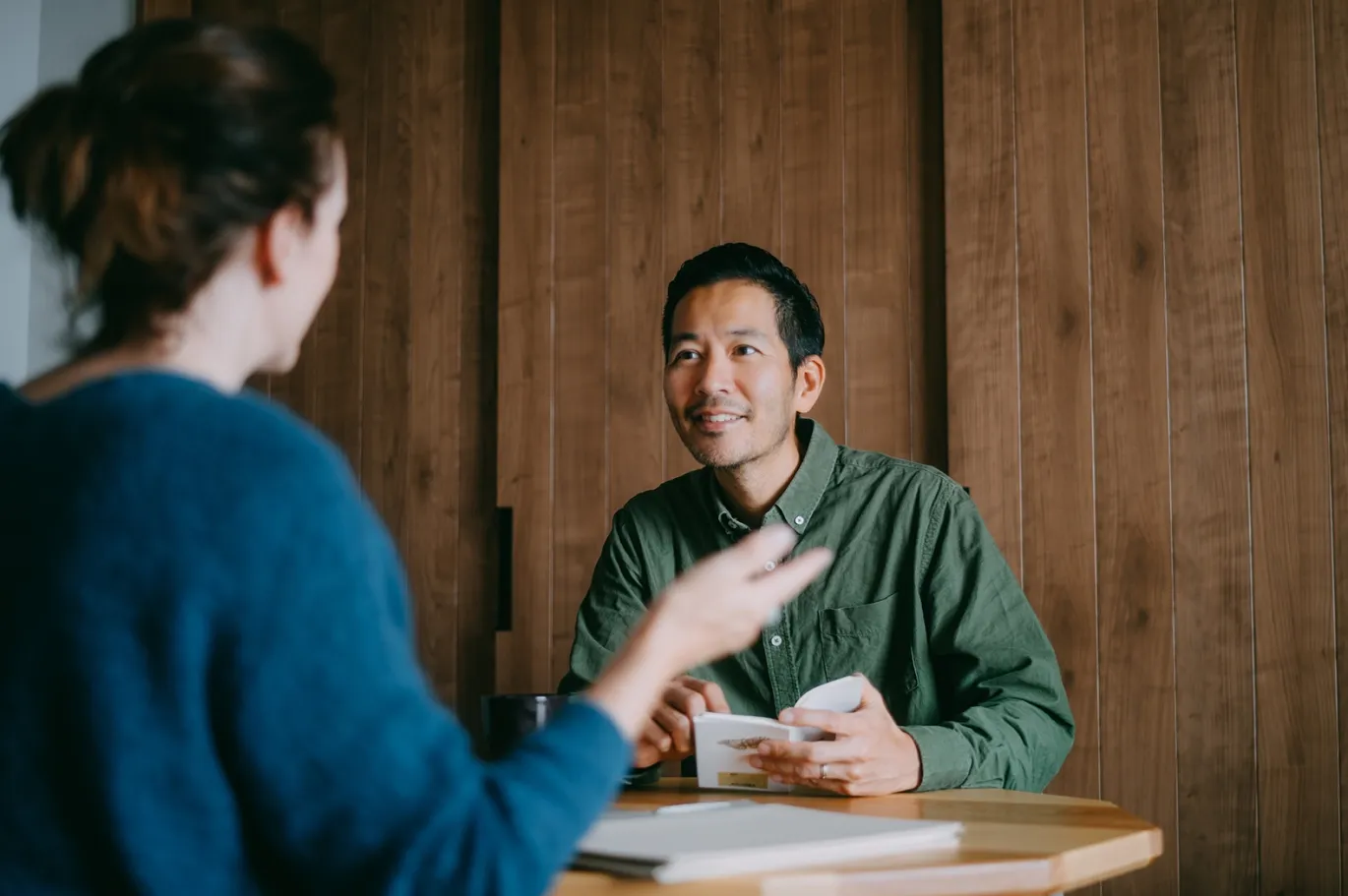 Two people having a discussion while sitting at a table indoors.