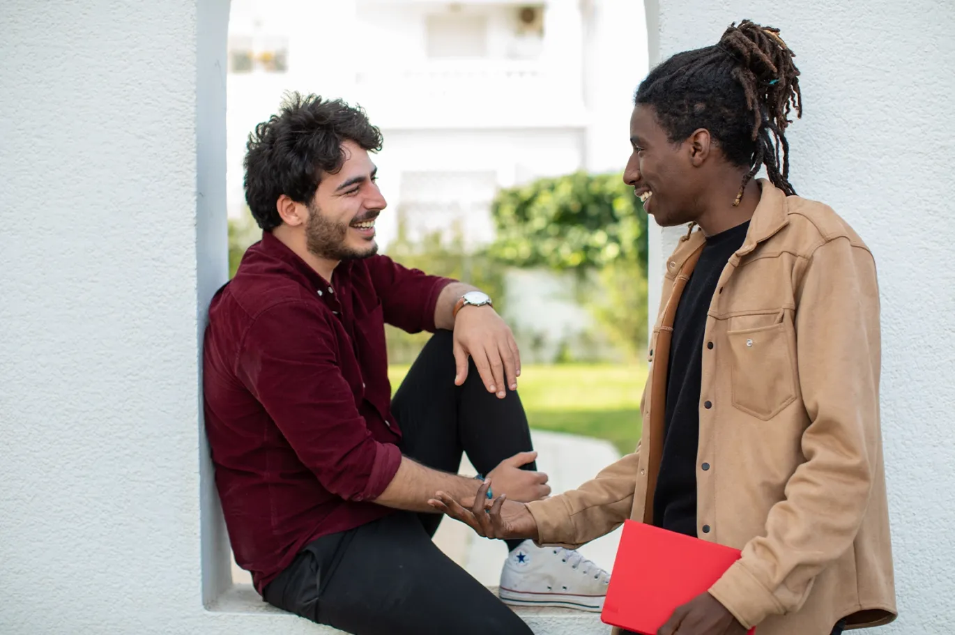 Two students talking together while holding study materials outdoors.