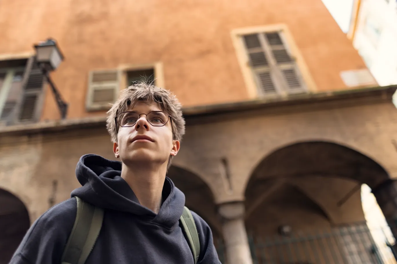 Young man with a backpack standing near a historic university building.