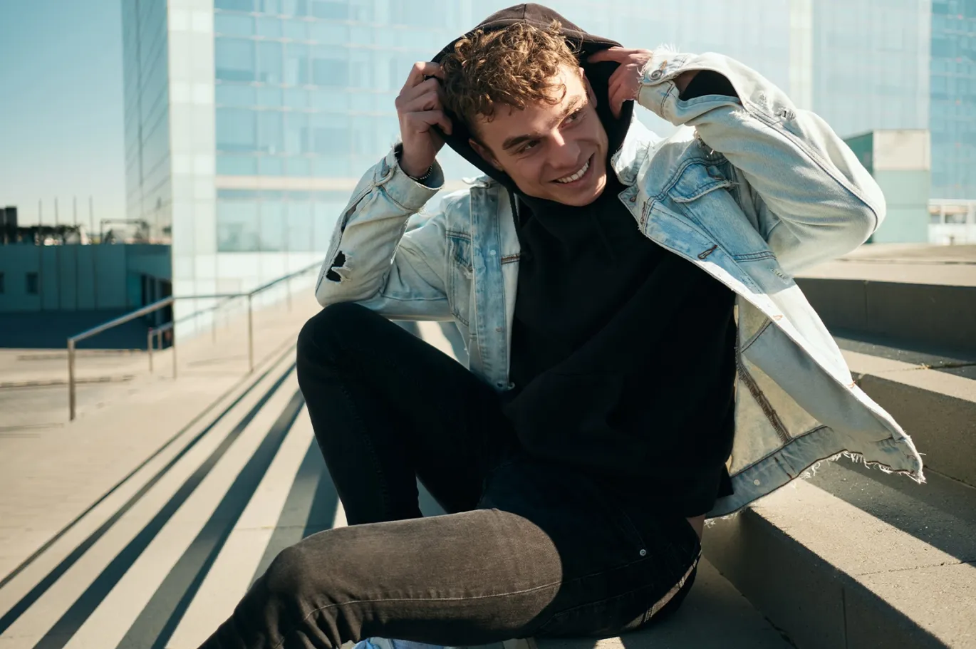 Young man adjusting his jacket while sitting outdoors in the city.
