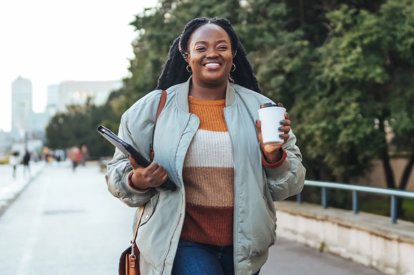Young woman with a backpack and coffee cup walking outdoors on a rainy day.