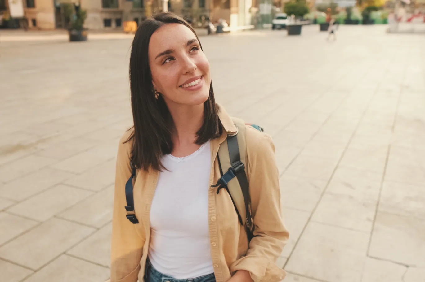 Young woman with a backpack smiling while standing outdoors in the city.