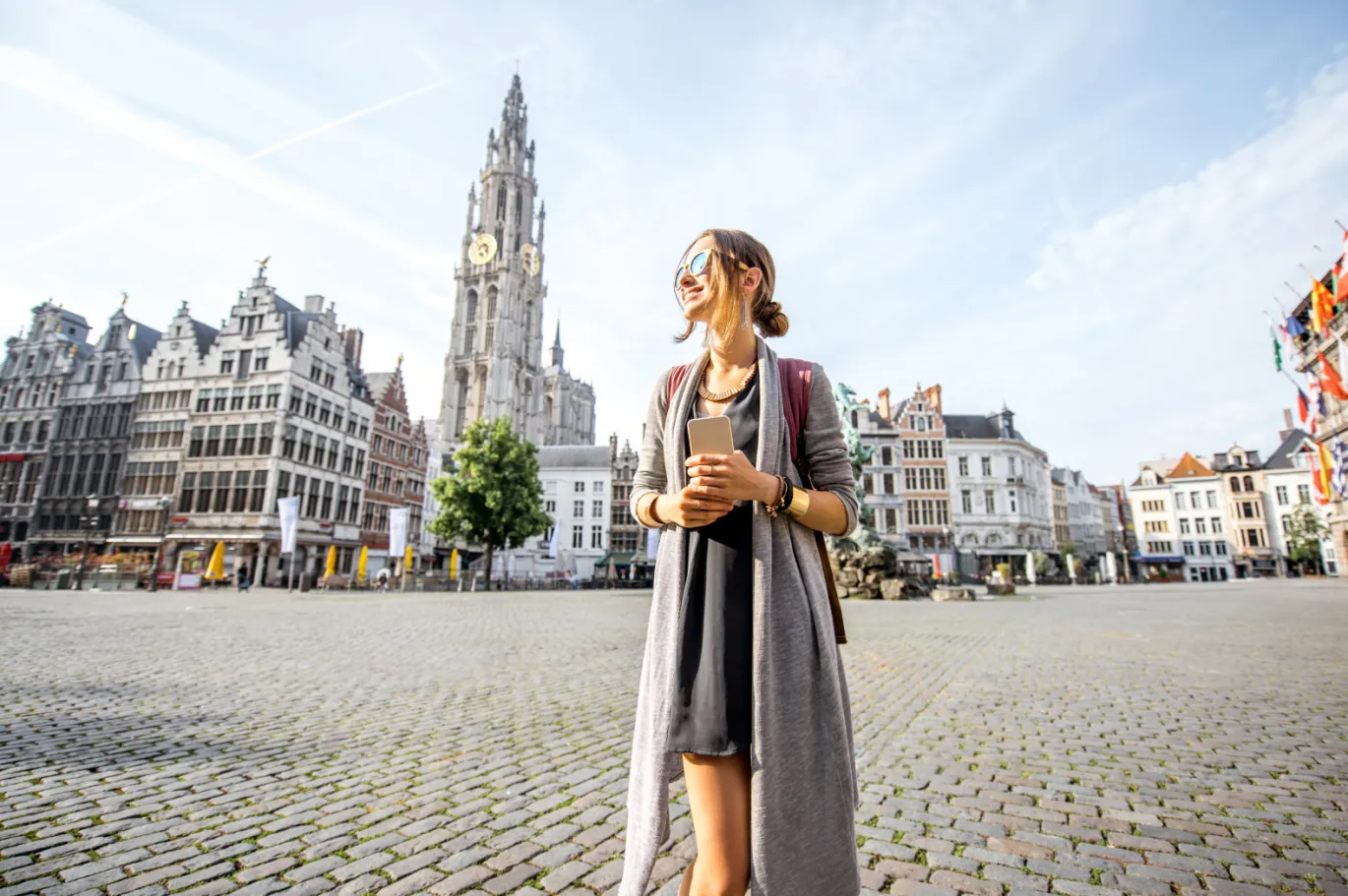 Young woman standing in a historic European city square with a coffee cup.