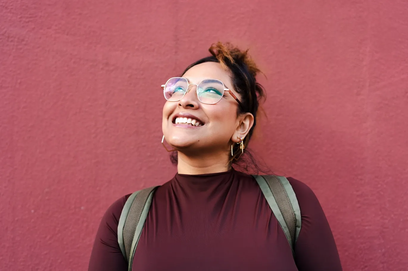 Young woman with glasses smiling while standing against a colorful wall.