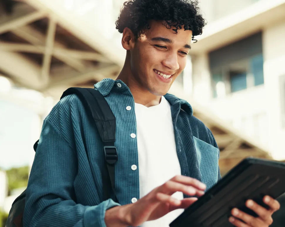 A man with backpack smiling while looking at a tablet