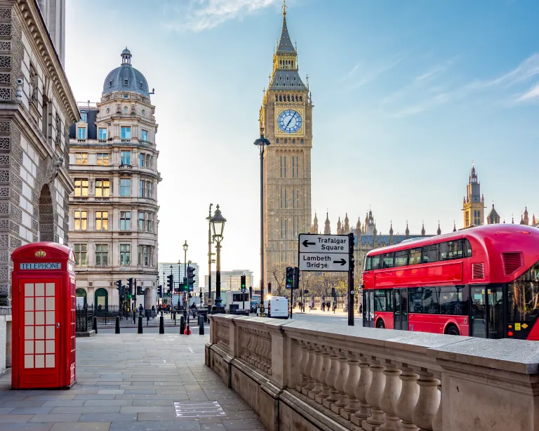 View of Big Ben and red double-decker buses on a London street.