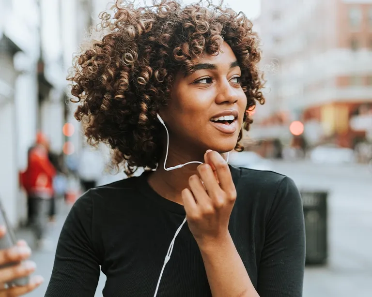 Curly-haired young woman listening to audio outdoors in the city.