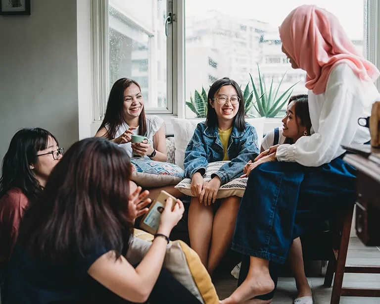 Group of girls sitting together and discussing IELTS study materials indoors.