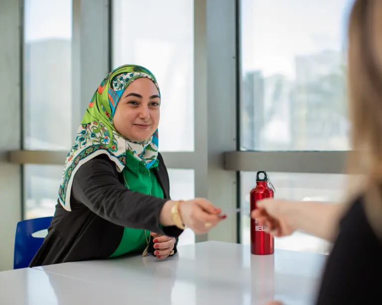 Student discussing documents with a staff member at an IELTS center reception desk.