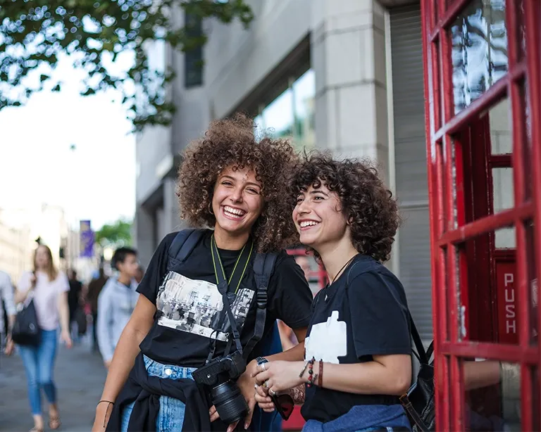 Two curly-haired friends smiling together on a city street.