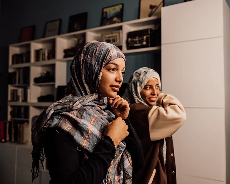 Two friends enjoying music together indoors while using headphones.