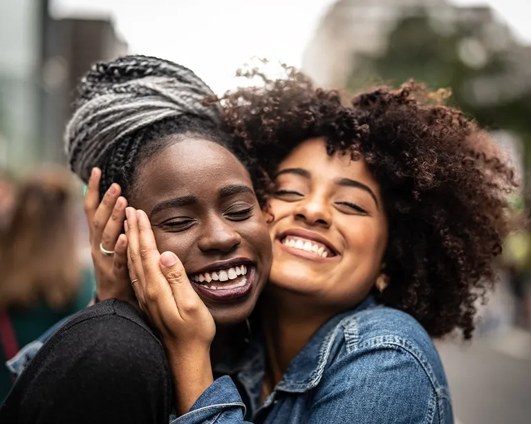 Two friends smiling and hugging together outdoors.