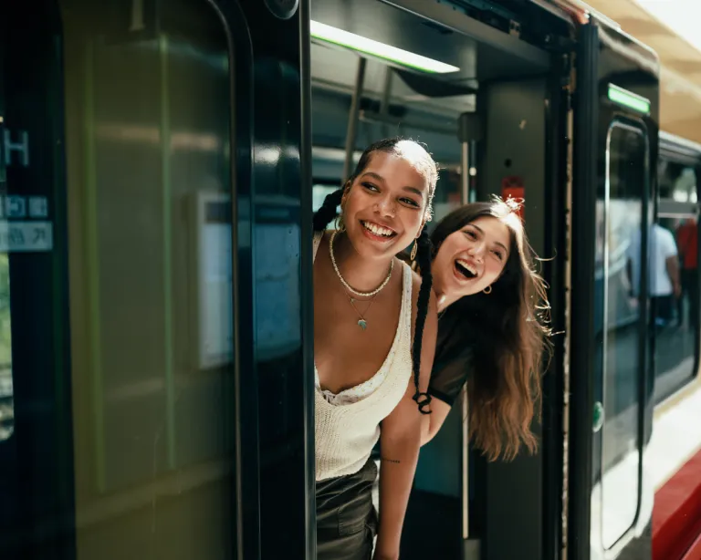Two friends smiling from the doorway of a metro train.