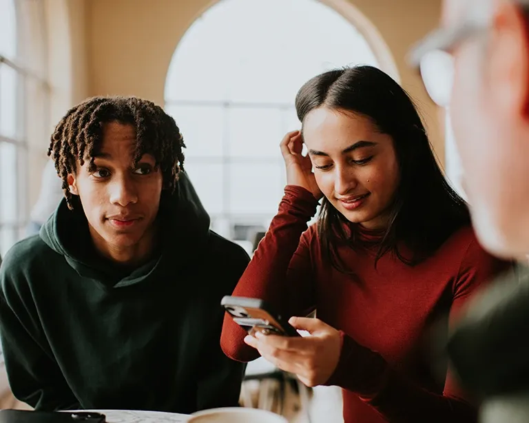 Two students discussing IELTS preparation together while using a mobile phone.