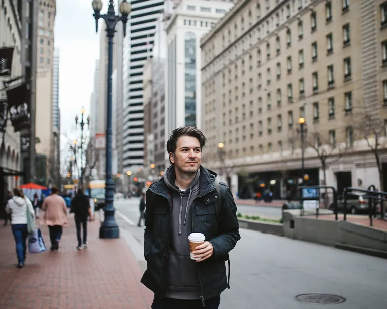 Young man with a backpack walking through a busy city street.