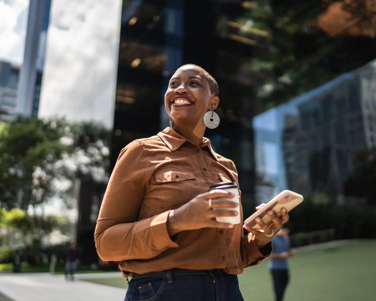Young man holding a coffee cup and mobile phone while standing outdoors in the city.