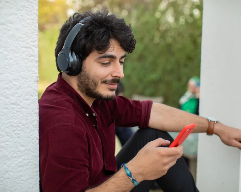 Young man with headphones using a mobile phone while relaxing outdoors.