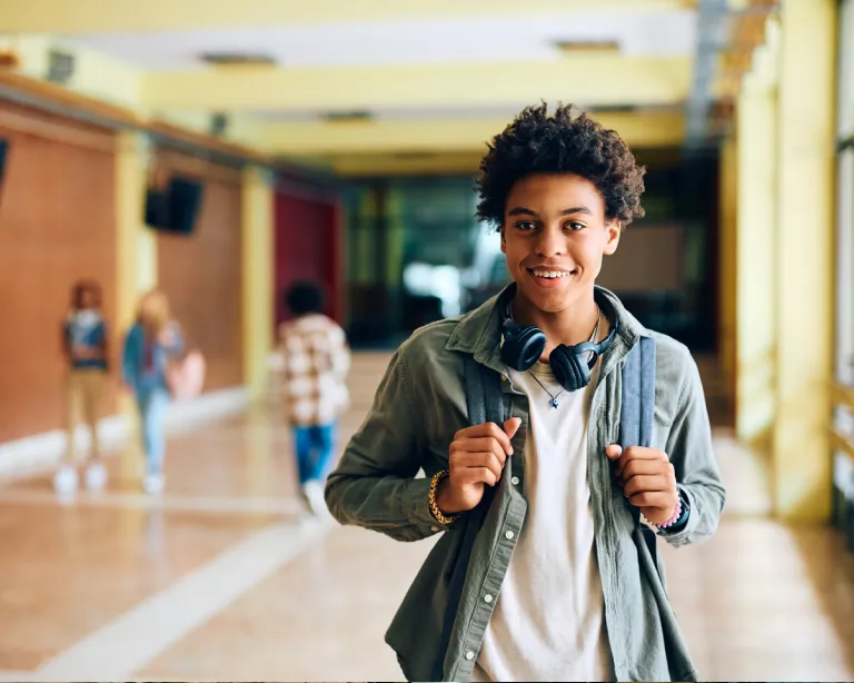 Young student with a backpack smiling inside a school hallway.