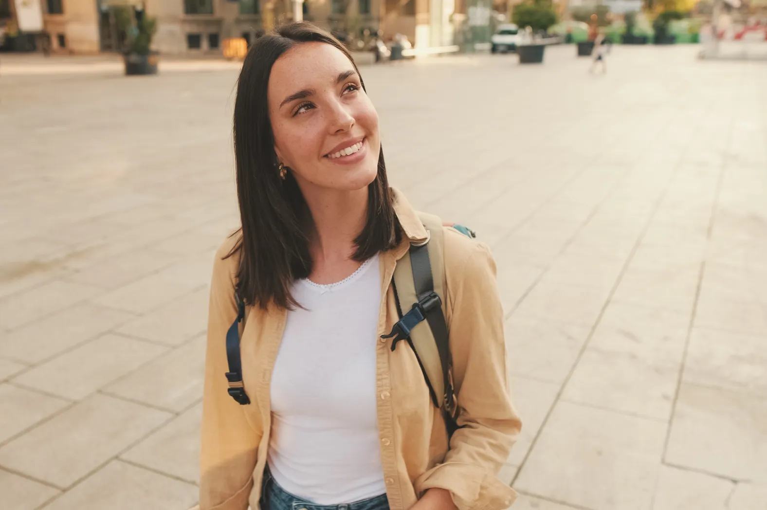 Young woman with a backpack smiling while standing outdoors in the city.