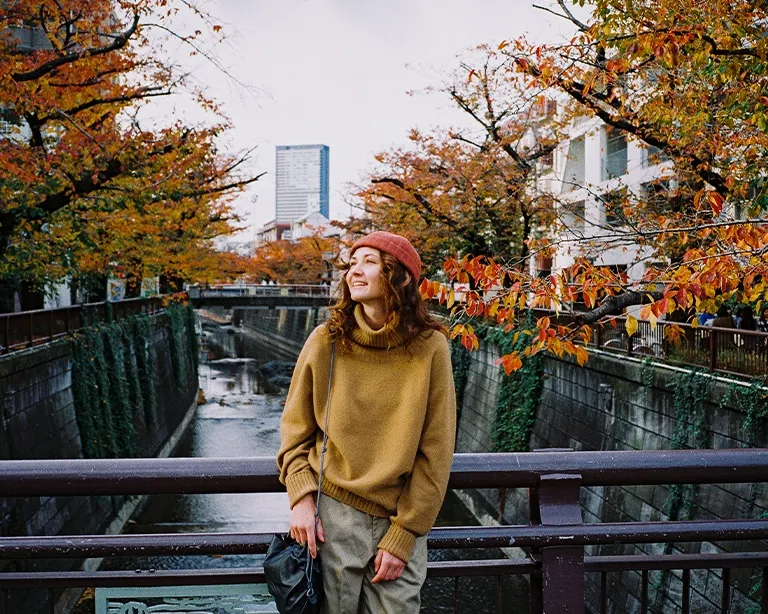 Young woman standing on a bridge surrounded by autumn trees in the city.
