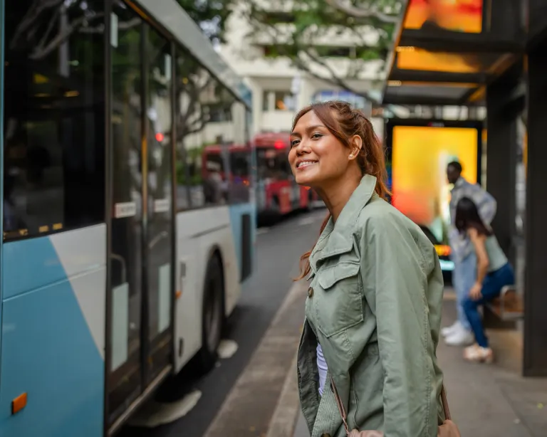 Young woman standing near a bus while using her mobile phone in the city.